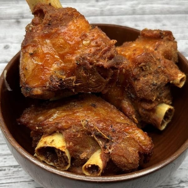 Three pieces of crispy, golden-brown fried meat with bones, served in a dark wooden bowl.