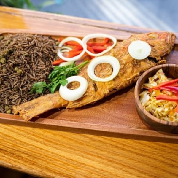 Fried whole fish with rice, onions, and peppers on a wooden tray.