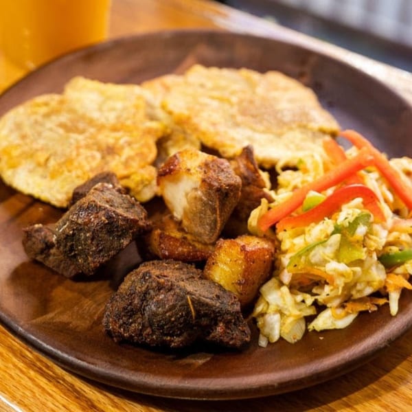 Haitian Blueline Fry plantain dish with fried meat, plantains, and coleslaw on a wooden plate.