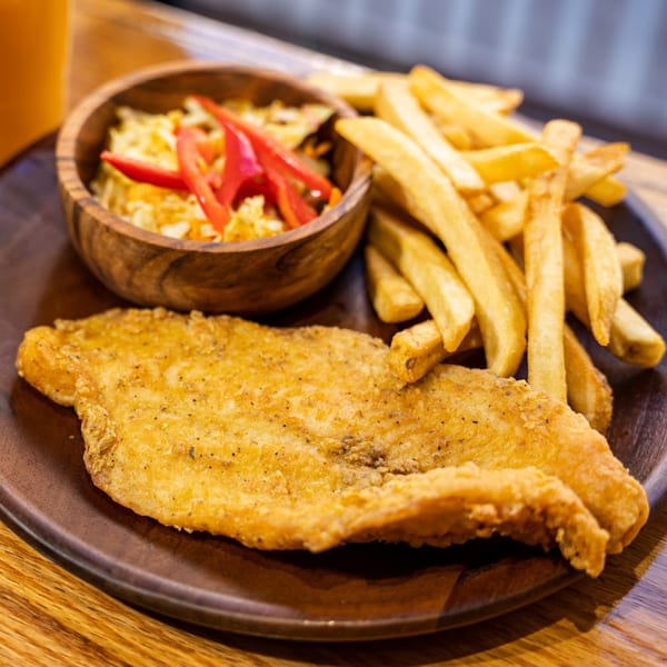Blueline Fry plantain, crispy fried fish, french fries, and coleslaw with red peppers on a wooden plate.